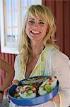 A smiling woman looking at the camera holding a plate with marinated fish.