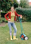 A woman leaning on a lawn-mower in a garden.