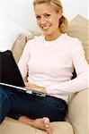 A smiling woman with a laptop in a sofa.