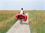 A man cykling carrying a rubber dinghy.