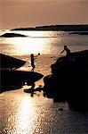Two children playing by the sea while the sun is setting.