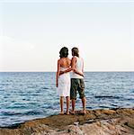 Young couple standing on a rock watching the ocean, Thailand.