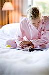 Une femme assise dans un lit en lisant un journal.