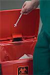 Healthcare professional placing used syringe in hazardous waste receptacle