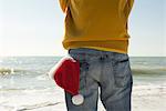 Man standing on beach looking at view, Santa hat in back pocket