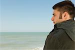 Young man at beach contemplatively looking at view