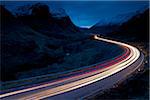 Spuren der Fahrzeugbeleuchtung in der Abenddämmerung durch bergige Tal Glen Coe, Schottland