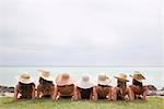 Women in straw hats recline by lake