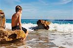 Boy sitting on rock looking out to sea