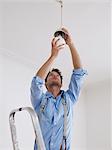 Young man on ladder screws in light bulb