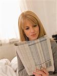 Young woman with newspaper in bed