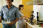 Couple in kitchen, woman cooking while man sets table