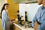 Couple talking together in kitchen as woman prepares food