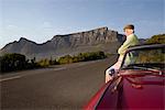 Senior homme admire la vue en se penchant sur vintage racing voiture sur Signal Hill, Cape Town, Afrique du Sud
