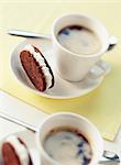 Chocolate and hazelnut shortbread biscuits filled with sugar ganache and cups of coffee