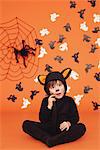 Boy In Cat Costume For Halloween Sitting Against Orange Background