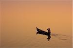 Myanmar, Burma, Amarapura. A fisherman paddling across Taungthaman Lake at sunrise, Amarapura.