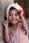 Myanmar, Burma, Mrauk U. Young village girl wearing a Christmas hat, her face decorated with thanaka, a local sun cream made from ground bark, Mrauk U, Rakhine State.