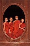 Myanmar, Burma, Nyaungshwe. Young novice monks standing at a wooden oval window, Shwe Yaunghwe Kyaung monastery.