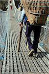 Nepal, Everest Region, Khumbu Valley.   Heavily laden porters cross wire suspension bridge on the Everest Base Camp Trek near Namche Bazaar