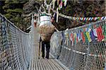 Nepal, Everest Region, Khumbu Valley. Heavily laden porters cross wire suspension bridge on the Everest Base Camp Trek near Namche Bazaar