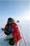 Norway, Finnmark Region. Dog sledding in the Arctic Circle - an explorer stops his husky team to make a phone call on a frozen lake.