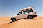 Oman, Wahiba Sands. A 4x4 eases over a sand dune in the midday sun.