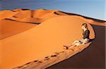 Oman, Empty Quarter. Une jeune femme montres le soleil descendre sur les dunes.