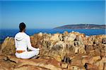 Woman practicing yoga on rocks, Plettenberg Bay, Western Cape, South Africa