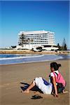 Woman relaxing on beach with Beacon Island Hotel in background, Plettenberg Bay, Western Cape, South Africa