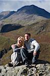 UK, North Wales, Snowdonia.  Couple sit on a rock in front of the Snowdon Horseshoe.