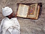 A Priest of the Ethiopian Orthodox Church reads a very old, beautifully illustrated bible beside the entrance to the rock hewn church of Yohannes Maequddi.The bibles script is Ge ez, the liturgical language of the Ethiopian Orthodox Church, which is comparable to Latin in the Roman Church.