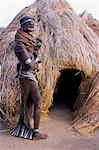 A Nyangatom woman stands with her baby on her hip beside her grass hut in his temporary camp. Nyangatom married women wear elaborately beaded skirts which reach the ground at the back and often have panels of different coloured calkfskin sewn into the tail  The Nyangatom or Bume are a Nilotic tribe of semi nomadic pastoralists who live along the banks of the Omo River in south western Ethiopia.