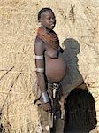 Une femme enceinte de Nyangatom en tenue traditionnelle à l'extérieur de sa maison au toit de chaume avec soin.Le Nyangatom sont une des plus grandes tribus et sans doute les plus belliqueuses de personnes vivant le long de la rivière Omo en Éthiopie.