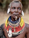 An old Turkana woman wearing all the finery of her tribe.In a hole pierced below her lower lip, she wears an ornament beautifully made from twisted strands of copper wire.Leaf shaped ear ornaments are typically worn by married women of the tribe and the tiny amber coloured rings hanging from her earrings are made from goats hooves.