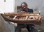 Mohamed Thuruani, a skilled craftsman of 17 years standing in Lamu, sits outside his home while putting the finishing touches to a model dhow.Dhow or Dau is the colloquial word used by most visitors for the wooden sailing ships of the East African coast.