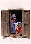 Un look jeune fille et l'enfant hors de la fenêtre avec volets d'une maison dans un joli village malgache du peuple Betsileo, qui vivent au sud-ouest de la capitale, Antananarivo.Most maisons construites par les Betsileo sont doubles étages avec une cuisine et d'habitation situé au premier étage.Bétail est souvent conservé au rez de chaussée d'une maison pendant la nuit.Les Betsileo sont gens industrieuses et expert riz loin