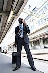 Ein Geschäftsmann mit einer Tasche mit einem Mobiltelefon bei einem Bahnhof, Stockholm, Schweden.