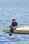 Jeune femme sur une jetée à l'aide d'un ordinateur portable, Suède.