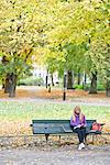 A woman sitting on a bench in a park using a laptop, Stockholm, Sweden.