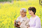 Middle-Aged Japanese Couple Photographing In Meadow