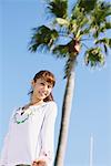 Junge Frau in der Nähe von einer Palme gegen blauen Himmel