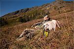 Male moose hunter rests on a sunny mountainside with his trophy moose antler rack in the Bird Creek drainage area, Chugach Mountains, Chugach National Forest, Southcentral Alaska, Autumn
