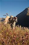 Orignal mâle chasseur s'arrête au verre la zone avec des jumelles comme il randonnées hors zone de chasse avec bois d'orignal trophée sur son pack, oiseau Creek bassin versant, les montagnes Chugach, forêt nationale de Chugach, centre-sud de l'Alaska, automne