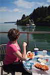 Woman watching fishing boats in the Near Island Channel while eating a seafood lunch at the Channel Side Chowder House in Kodiak, Kodiak Island, Southwest Alaska, Summer