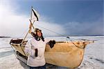 Mâle chasseur Inupiaq Eskimo, debout à côté d'un Inupiaq Umiaq fait de peau de phoque barbu (Ugruk) tout en portant une parka traditionnelle des Esquimaux (Atigi) et seal skin hat, mer des Tchouktches près de Barrow, Alaska arctique, été