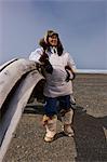 Male Inupiaq Eskimo hunter standing behind a Bowhead whalebone along the Chukchi Sea wearing his Eskimo parka (Atigi), seal skin hat and wolf skin Maklak's with soles made from bearded seal skin (Ugruk),  Barrow, Arctic Alaska, Summer