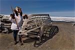 Männlich Inupiak Eskimo Jäger tragen seine Eskimo Parka (Atigi), Dichtung Haut Hut und Wolf Maklak der Haut mit Sohlen aus Bartrobbe Haut (Ugruk) Stand vor eine Bowhead Wal-Knochen-Bogen und Umiaqs, Barrow, Alaska Arctic Sommer gemacht