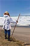 Portrait d'un chasseur Inupiaq Eskimo mâle portant son parka Eskimo (Atigi) et un chapeau de peau de phoque et tenant un bâton de marche à Utkeagvik ancien lotissement original avec vue sur la mer des Tchouktches, Barrow, Alaska arctique, l'été