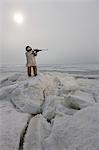 Female Inupiaq Eskimo hunter wearing a Eskimo parka(Atigi) aims a rifle towards the open water of the Chukchi Sea, Barrow, Arctic Alaska, Summer